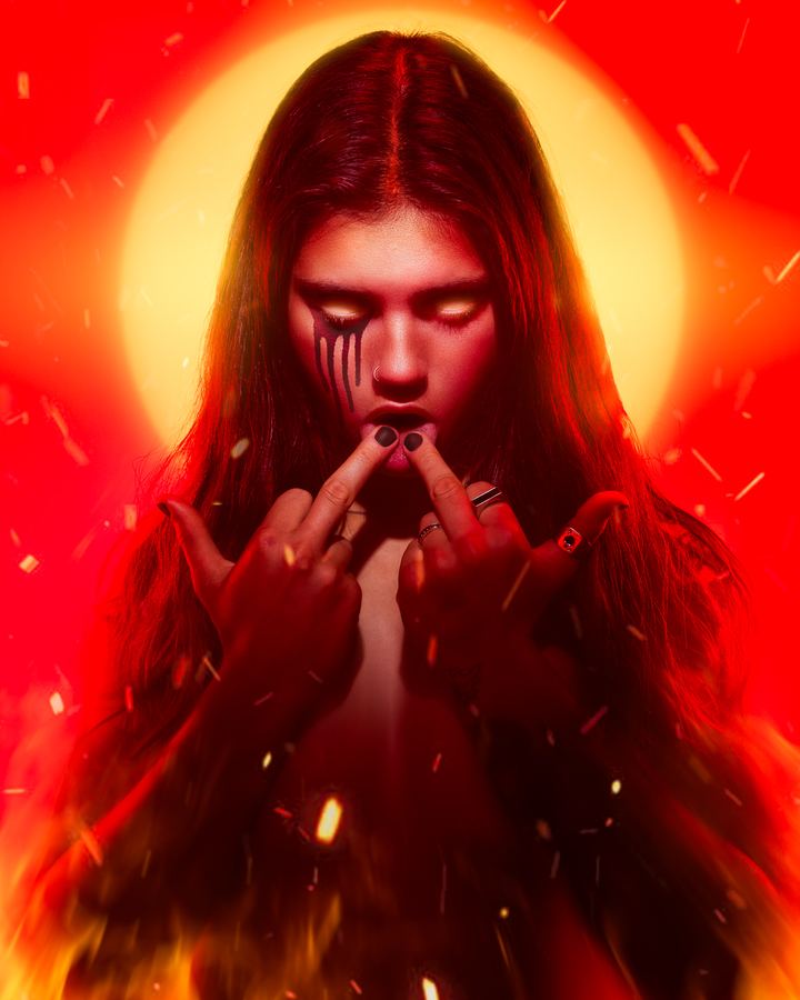 Saint Ash: Black tears and a burning halo: a long-haired figure in red, embers rising