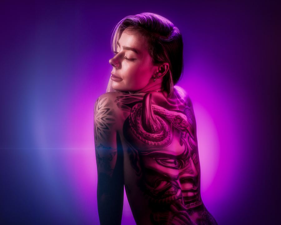 Ink Tide: A tattooed back and shoulder turned to the camera in violet and magenta light