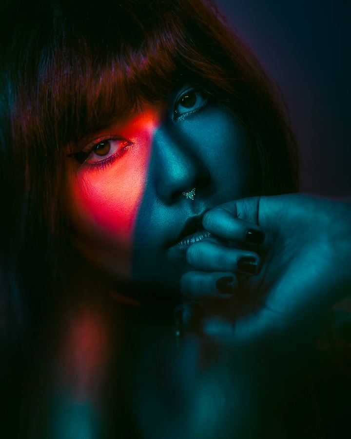 Hush: Half the face in red, half in teal, a hand resting on the lips