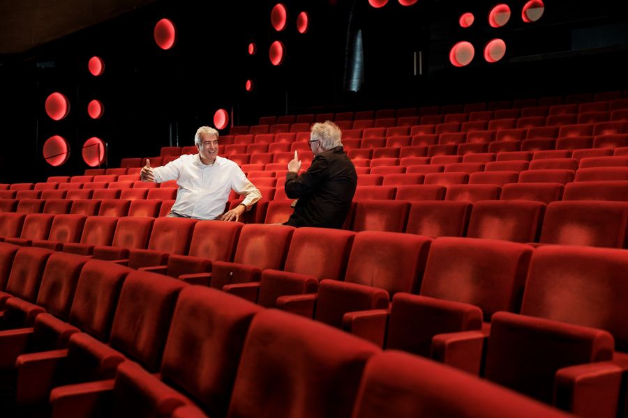 Two men talking across a row of empty red theatre seats