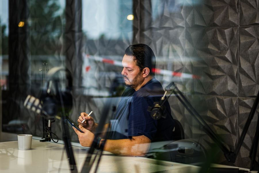 A podcast host at the microphone, photographed through the studio window