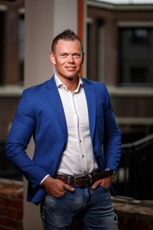 An entrepreneur in a blue blazer, hands in pockets, a brick courtyard behind