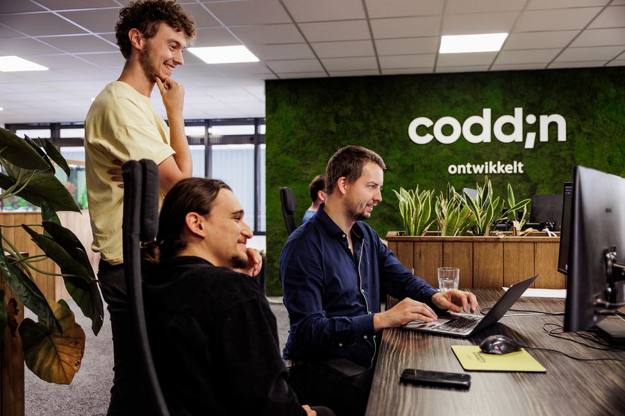 Three developers at one screen in front of the Coddin moss wall