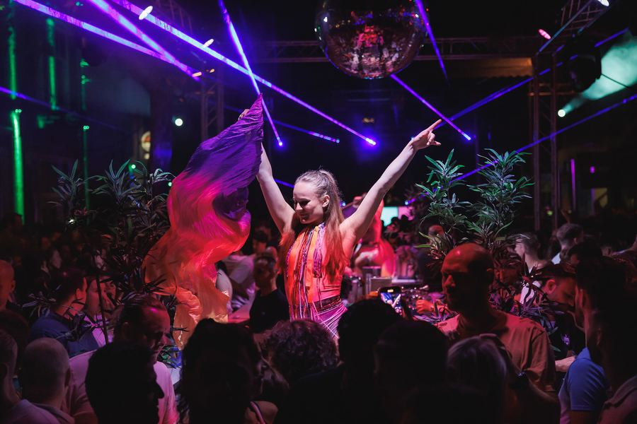 A dancer pointing into the lasers under a mirror ball, the crowd below