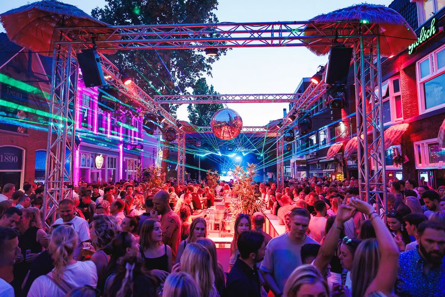 Street festival at dusk: a truss stage, green lasers and a mirror ball over the crowd