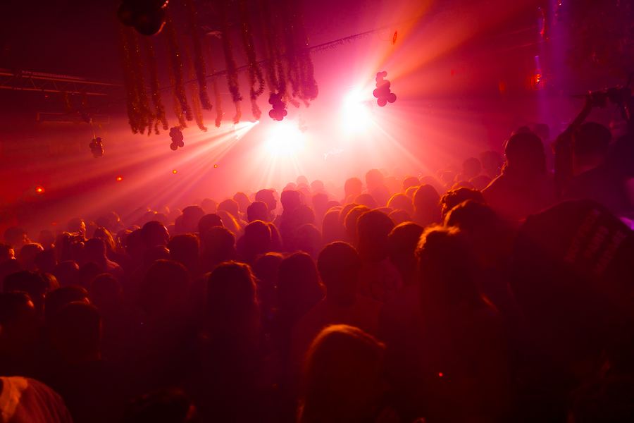 A crowd in silhouette against red stage beams