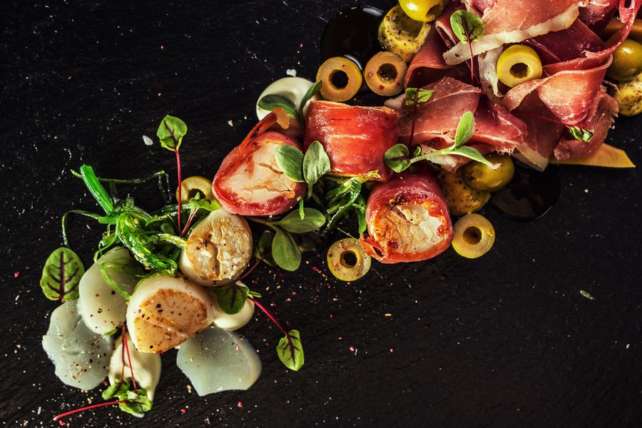 Scallops, cured ham and green olives scattered across black slate