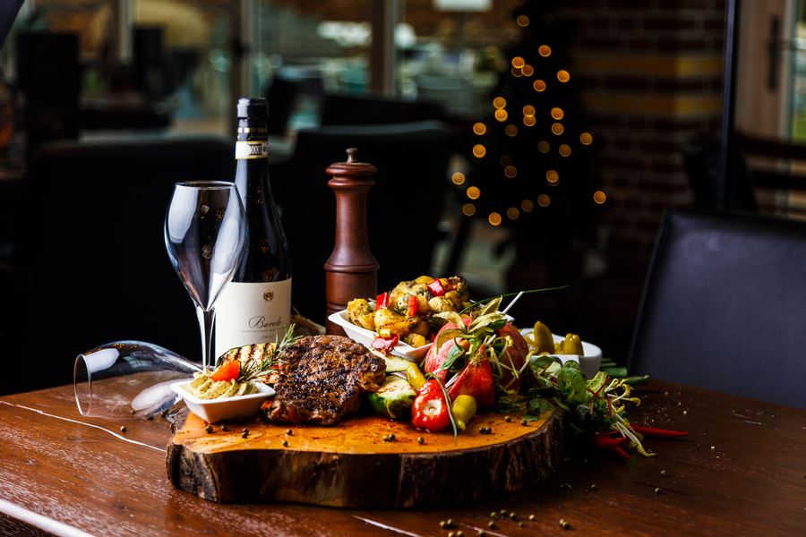 Grilled steak and vegetables on a tree-slice board, wine alongside