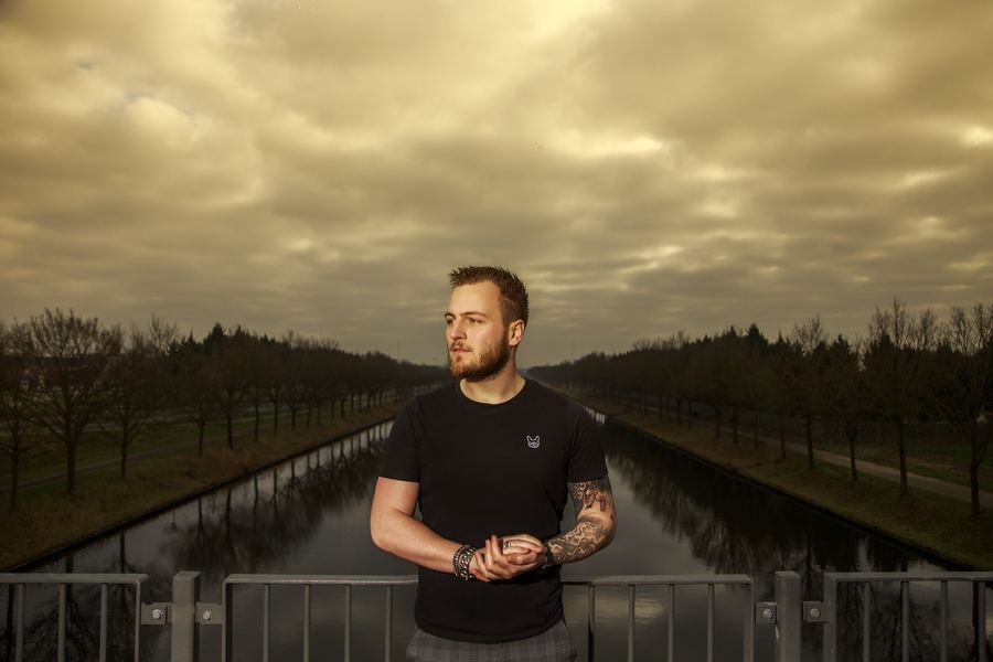 Tattooed arms folded on a bridge rail, a canal running away under heavy cloud
