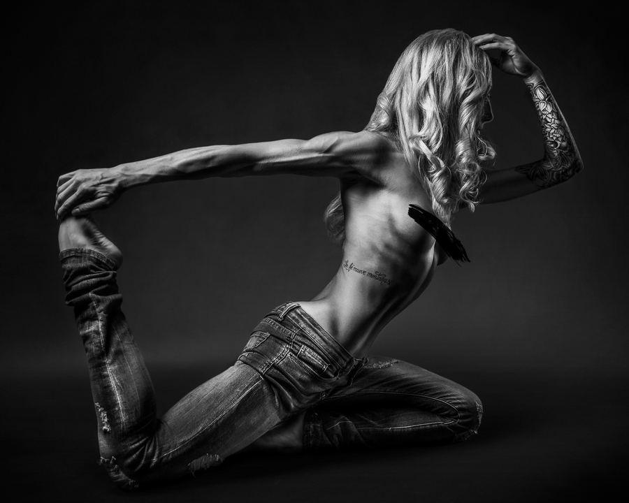 A dancer folded into a bow pose, every muscle lit, in black and white