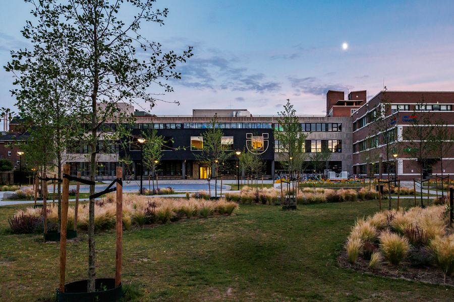 A campus lawn and brick buildings at twilight, the moon above