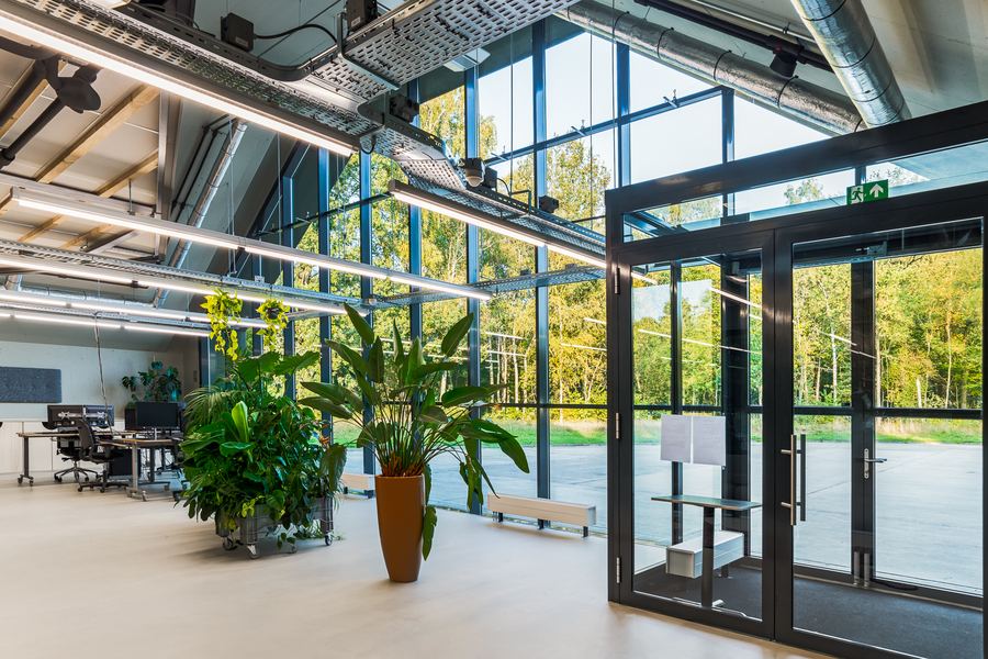 A double-height workspace behind a full glass wall, trees outside