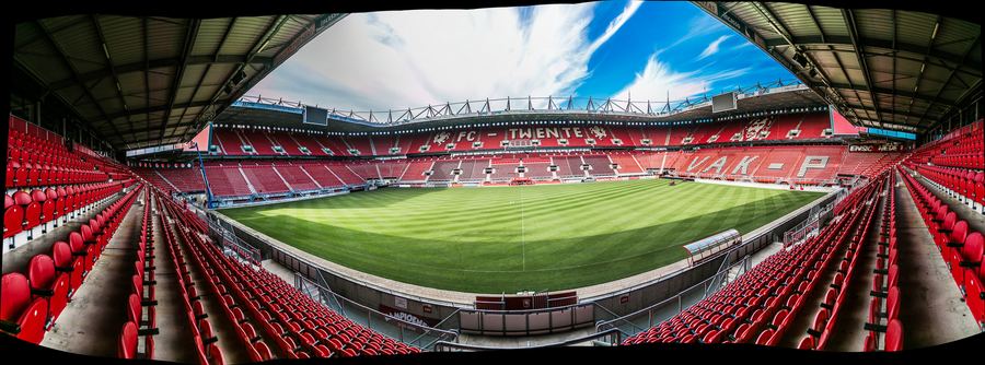 Panorama of an empty football stadium, red stands around a striped pitch