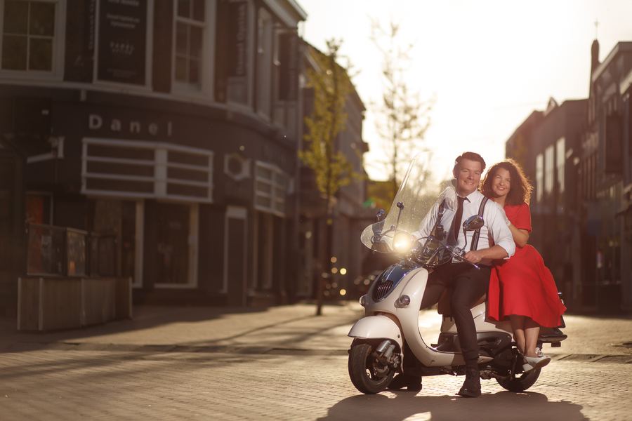 On a white Vespa in the evening sun, red dress and braces