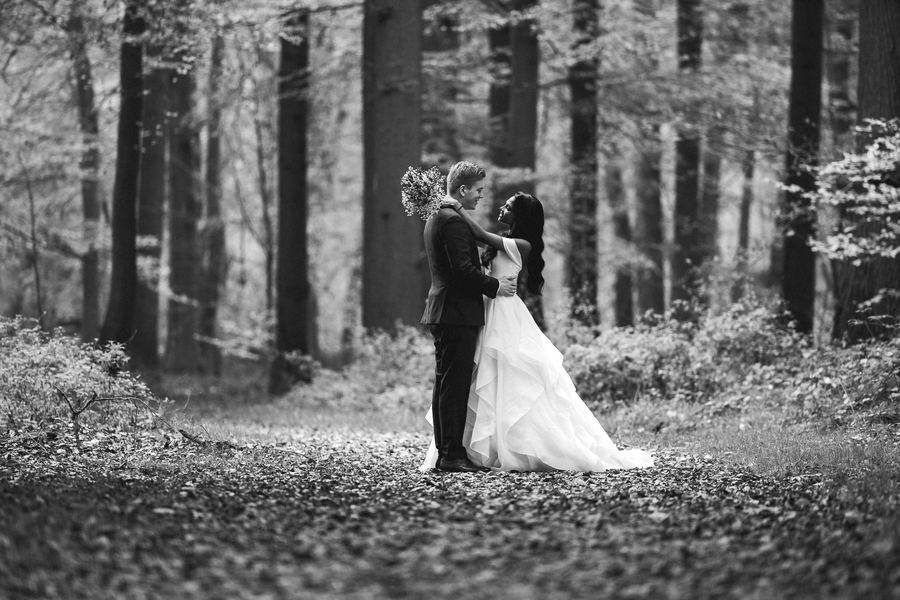 Bride and groom small among tall trees, in black and white