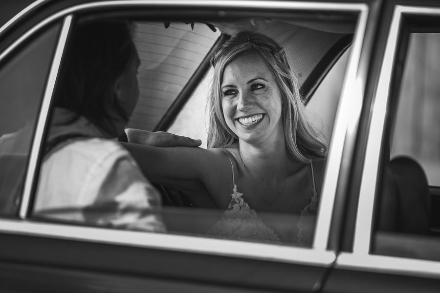 The bride laughing through the window of the wedding car, in black and white