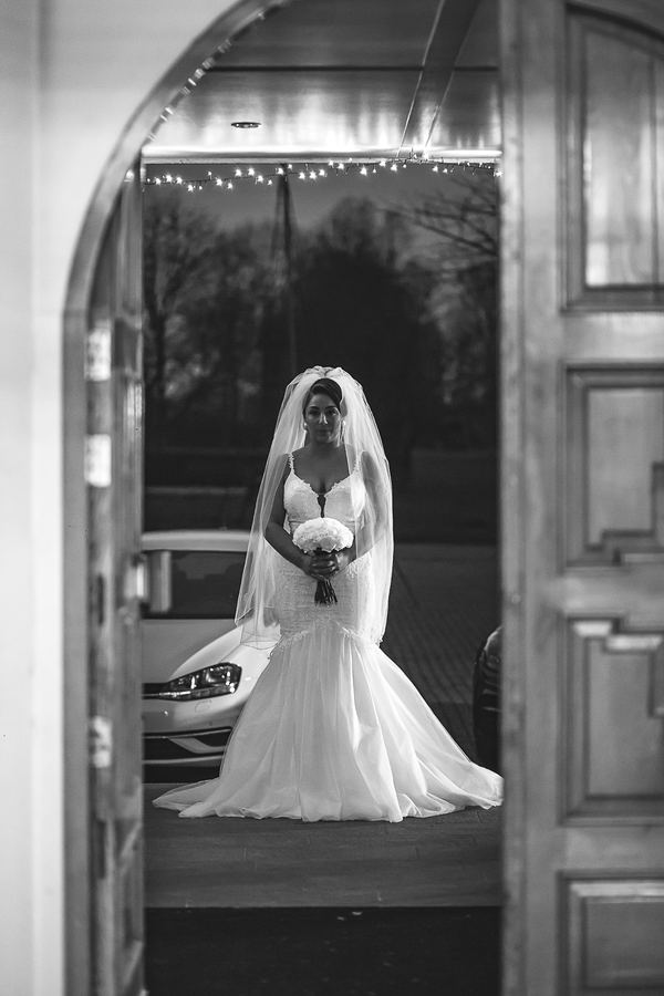 The bride framed in an arched doorway, veil down, in black and white